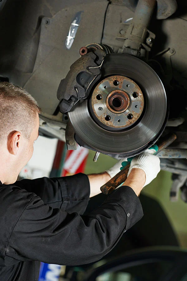 Technician inspecting a brake rotor and suspension on a lifted vehicle
